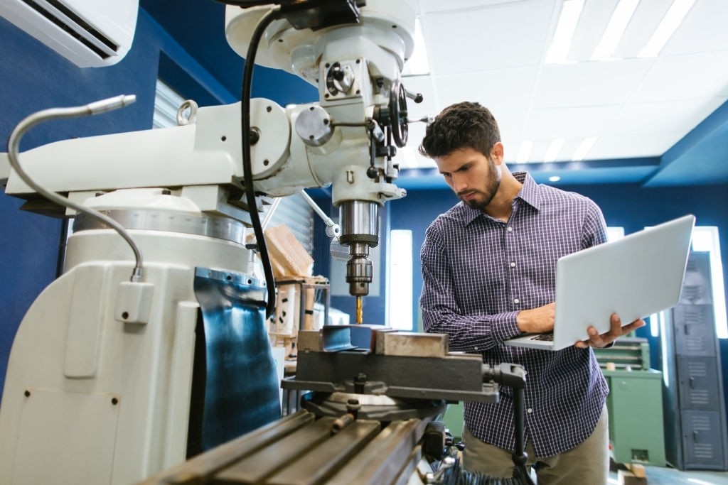 A young latin engineer calibrating a large drill with his laptop in his shop