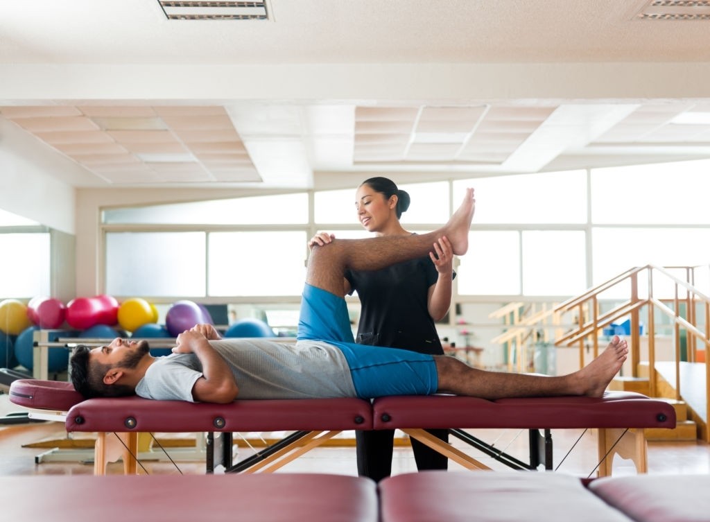 Male patient lying on massage table with leg held by massage therapist