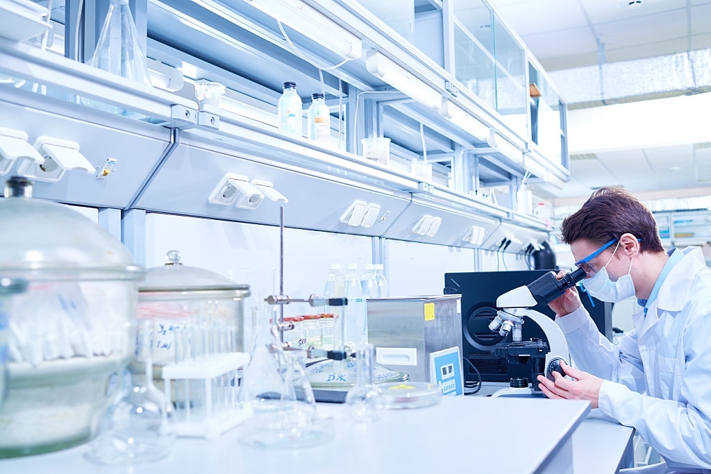 Young scientist examining sample with microscope in modern laboratory