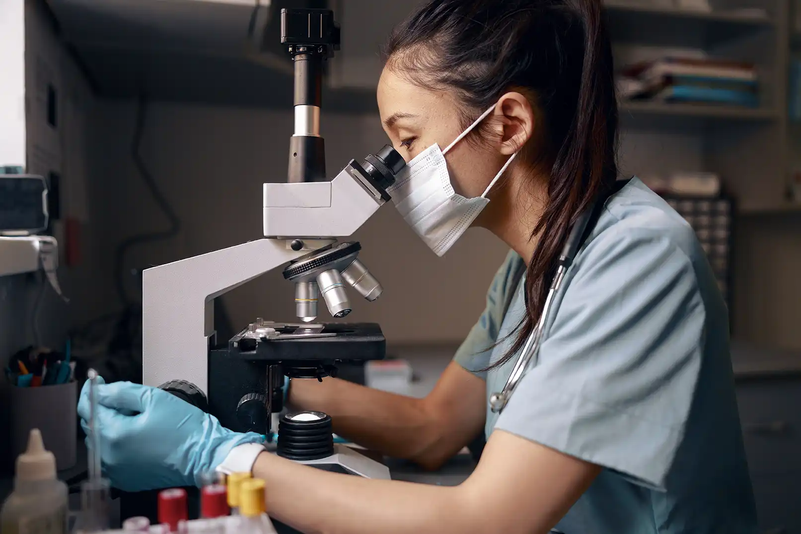 asian woman with medical mask looks into microscope